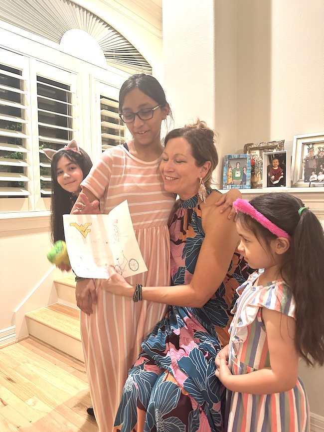 Picture of author Sara reading a birthday card surrounded by her three grandchildren
